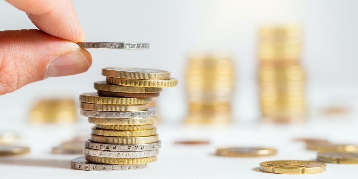 Hand adding a coin on pile of euros with others stacked in background